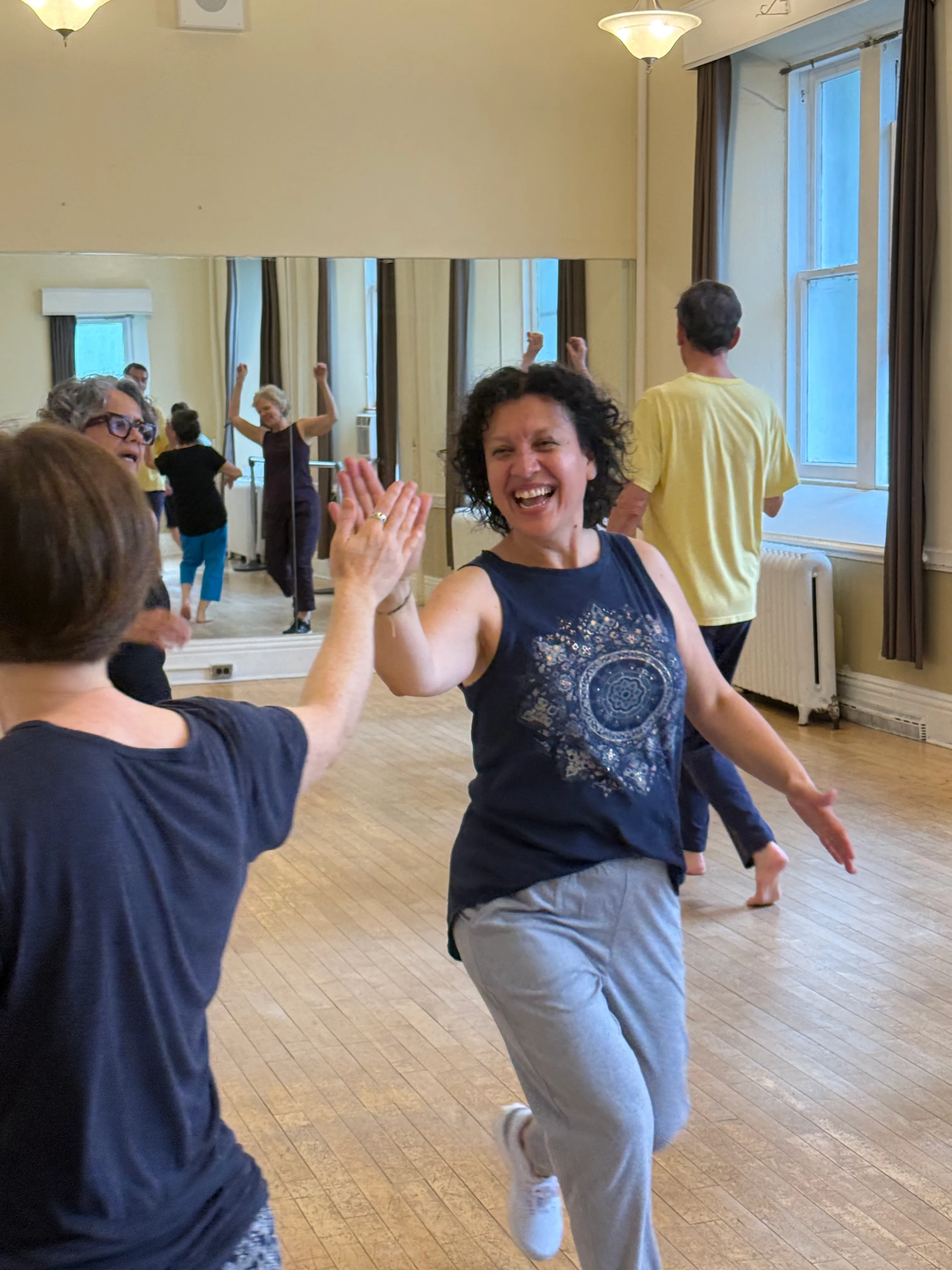 Diana laughing mid-movement in a Biodanza class, arms open among a circle of dancers