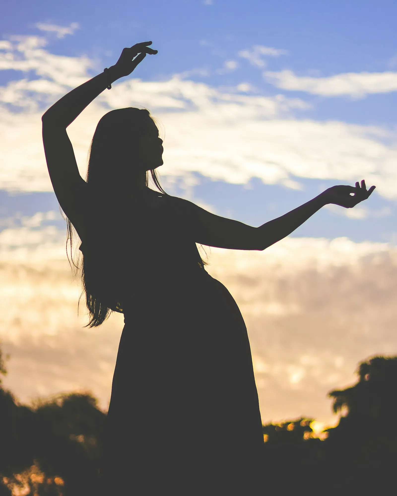 A figure silhouetted against an evening sky, arms lifted mid-movement