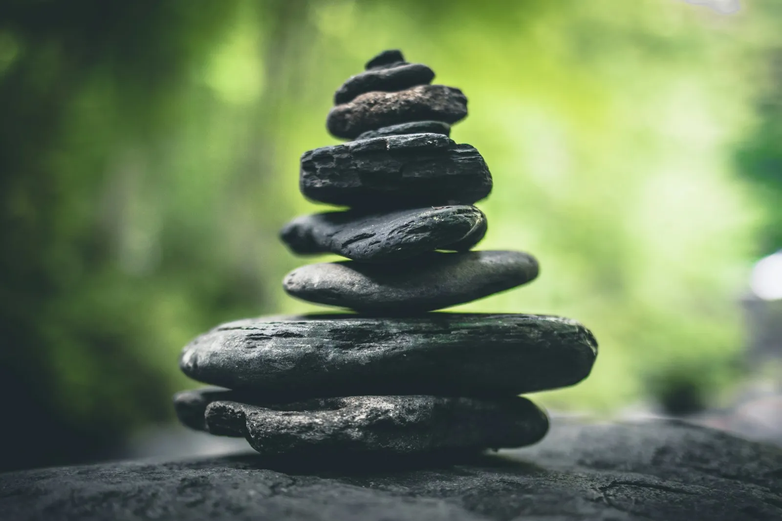 A stack of smooth flat stones balanced in front of soft green foliage
